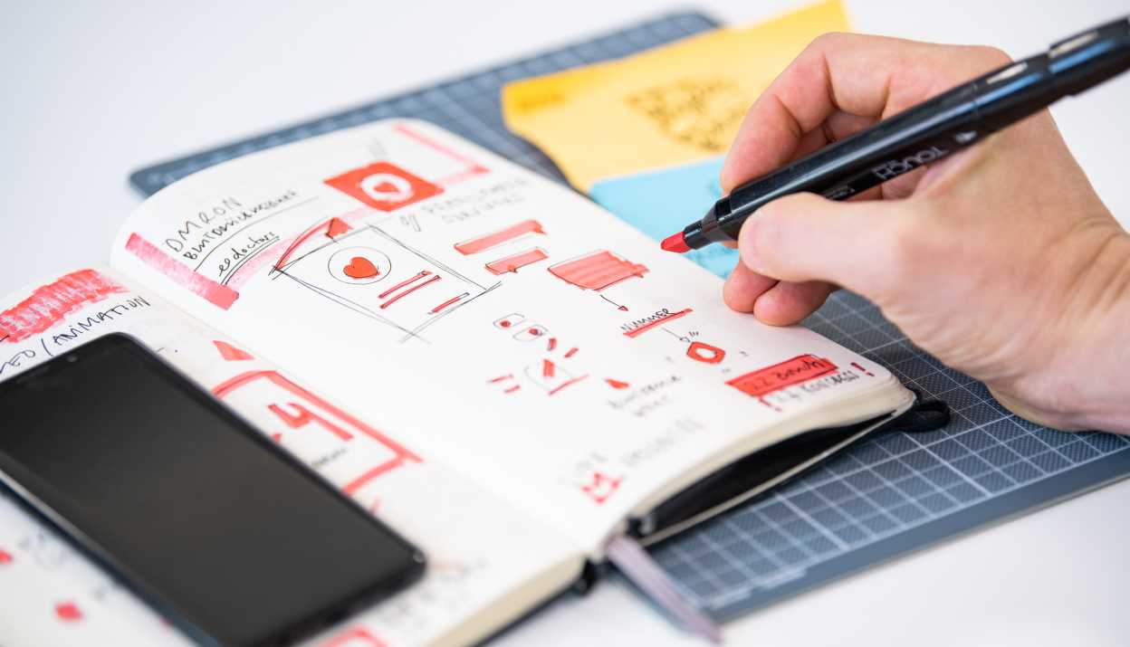 Carnet de notes avec des esquisses dans lequel une main dessine quelque chose avec un marqueur de couleur