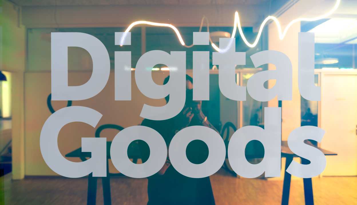 Schriftzug "Digital Goods" fotografiert vor einem farbig spiegelnden Fenster