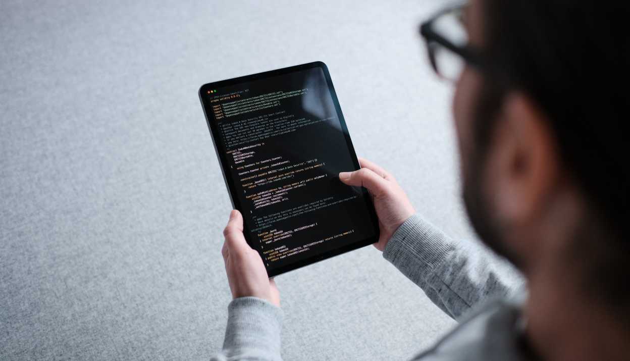 Person hält iPad in Händen, auf welchem ein Teil eines Smart Contract Codes angezeigt wird