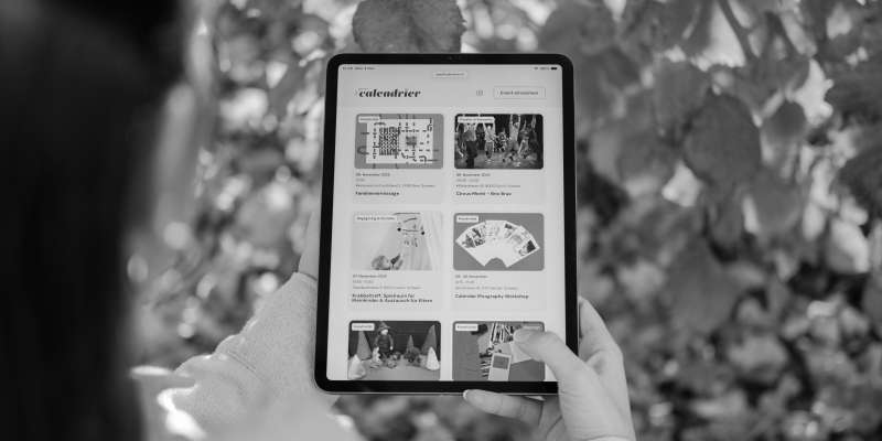 Le petit calendrier wird auf einem Tablet angeschaut, im Hintergrund sind Blätter eines Baumes