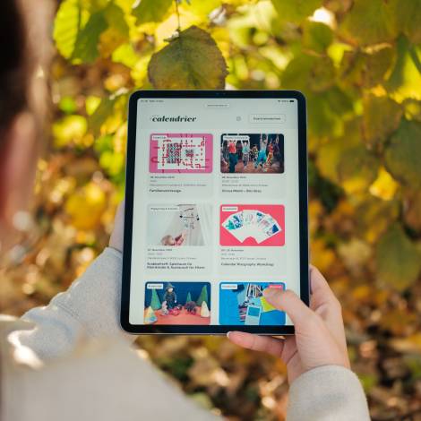 Le petit calendrier wird auf einem Tablet angeschaut, im Hintergrund sind Blätter eines Baumes