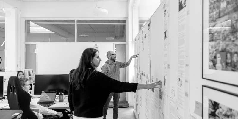 Das Marketing und Sales Team schaut gemeinsam Texte an, die an einer Wand im Büro aufgehängt sind.