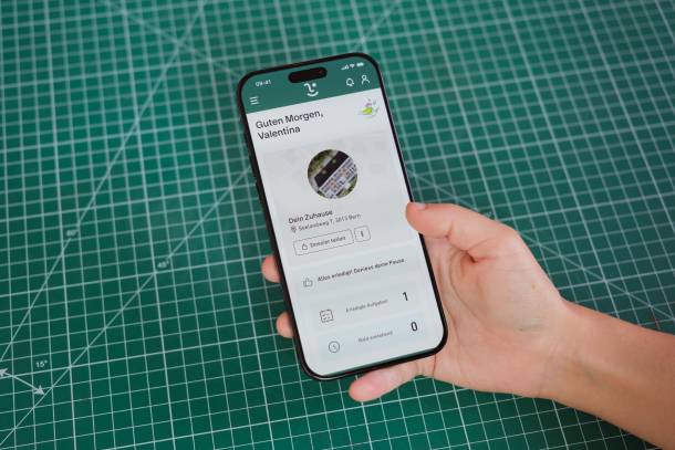 Homescreen der myky App geöffnet auf einem Smartphone in der Hand einer Person vor einer grünen Schneidematte mit weissem Raster
