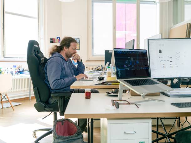 Olivier Oswald arbeitet am Laptop. Im Vordergrund sind mehrere Monitore mit geöffneten Programmen. Im Hintergrund befindet sich ein grosses Fenster.