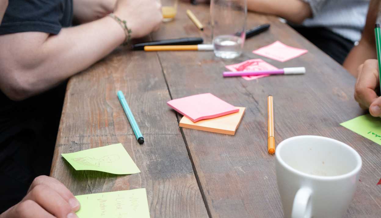 Leute sitzen an einem Holztisch und schreiben auf farbige Post-its