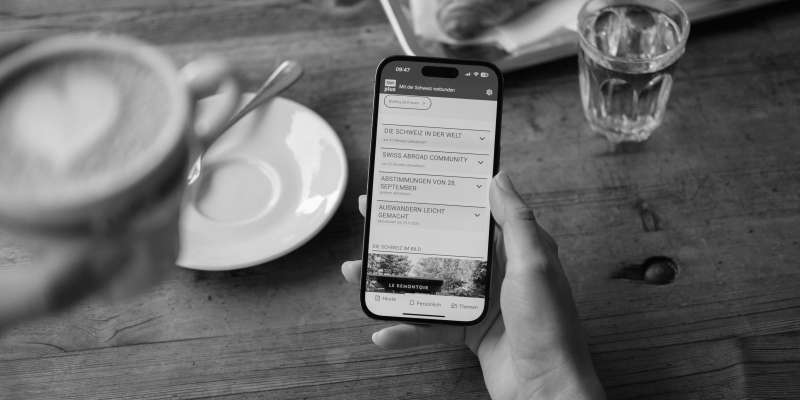 SWIplus App geöffnet auf einem Smartphone in der Hand einer Person, die Kaffee trinkt